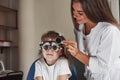 Doctor is tuning the device. Little girl in glasses sitting in clinic and having her eyes tested