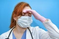 The doctor in a uniform on a blue background tiredly bowed her head, copy space. Sad nurse face with glove and medical mask