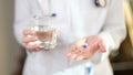 Doctor in uniform holds pill and glass of water in hands