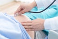 Doctor using hands and stethoscope listening to patient, pregnant tummy for health check up