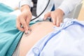 Doctor using hands and stethoscope listening to patient, pregnant tummy for health check up