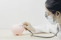 Doctor ware madical mask and using stethoscope to check illness of pink piggy bank. Concept check saving money and financial Royalty Free Stock Photo