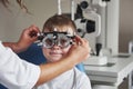 Doctor wear glasses to a kid. Little boy with phoropter having testing his eyes in the doctor`s office