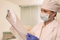 Doctor wearing face mask and cap while examining medical result at clinic