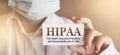 Doctor wearing face mask shows a card with the text HIPPA, The Health Insurance Portability and Accountability Act of 1996,.