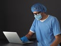 Doctor wearing mask, gloves and blue uniform using laptop Royalty Free Stock Photo