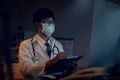 The doctor wearing mask is sitting at a desk at the night, Which is researching how to treat the patient`s condition. Royalty Free Stock Photo