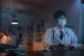 The doctor wearing mask is sitting at a desk at the night, Which is researching how to treat the patient`s condition. Royalty Free Stock Photo