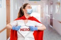 The doctor, wearing medical mask, gloves and a superhero Cape, tears open the coat, showing the inscription on the chest of the