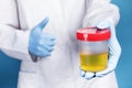 A doctor in a white coat and blue gloves holds a plastic can of urine in hand. urine tests virus, pregnancy, diseases