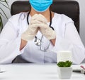 Doctor in a white coat and blue latex gloves sits at a white work table in his office, concept of patient reception in the clinic