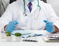 Doctor in a white coat and blue latex gloves sits at a white work table in his office, concept of patient reception in the clinic