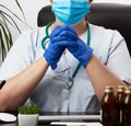 Doctor in a white coat and blue latex gloves sits at a white work table in his office, concept of patient reception in the clinic