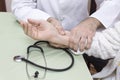 Doctor in a white coat examines the pulse on the wrist of an old woman in a white bathrobe. The stethoscope is on the table