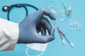 Doctor in a white coat holding glass ampoule. Hand in a blue sterilized surgical glove. Blurred background with medical tools