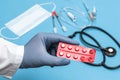 Doctor in a white coat holding tablets in red blister. Hand in a blue sterilized surgical glove. Blurred background with medical Royalty Free Stock Photo