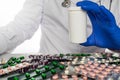 Doctor in white coat sits infront of pill boards scattered on table holding up blank prescription bottle. Royalty Free Stock Photo