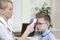 Doctor in a white coat and a stethoscope around the neck is sitting in the doctor`s office. He measures the temperature of the boy