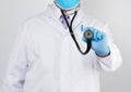 Doctor in a white coat and tie holds in his hand a black phonendoscope