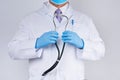 Doctor in a white coat and tie holds in his hand a black phonendoscope, wearing blue sterile gloves
