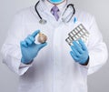 Doctor in a white medical coat and blue rubber gloves holds a fresh head of garlic and pills Royalty Free Stock Photo