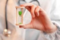 A doctor in white medical gloves holds an hourglass - a symbol of time to heal and cure. Close up