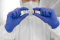 Doctor in white protective suit, medical mask and rubber gloves is holding a red and white pill as a medications from