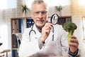 Doctor sitting at desk in office. Man is looking at broccoli with magnifying glass.