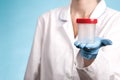 Doctor in a white uniform and blue gloves on blue background holds an empty plastic test jar