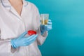 Doctor in white uniform and blue gloves on blue background holds plastic test jar with yellow urine. test for disease