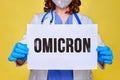 A doctor in a white uniform holds a sheet of paper with the text of the new variant covid virus Omicron, yellow background Royalty Free Stock Photo