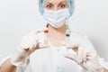 Doctor woman in face mask, sterile hat, gloves holding liquid medicine in bottle with syringe with needle isolated on Royalty Free Stock Photo