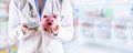 Doctor woman hands holding pills and piggy bank. Blurred pharmacy interior in the background Royalty Free Stock Photo