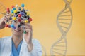 Doctor woman holding a medical figure with 3D DNA strand against yellow background Royalty Free Stock Photo