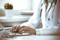 Doctor woman using laptop computer while sitting at the desk near window in hospital. Medicine and health care concept Royalty Free Stock Photo
