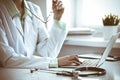 Doctor woman using laptop computer while sitting at the desk near window in hospital. Medicine and health care concept Royalty Free Stock Photo