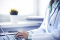 Doctor woman using laptop computer while sitting at the desk near window in hospital. Medicine and health care concept Royalty Free Stock Photo