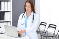 Doctor woman at work. Portrait of female physician using laptop computer while standing near reception desk at clinic or Royalty Free Stock Photo