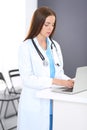 Doctor woman at work. Portrait of female physician using laptop computer while standing near reception desk at clinic or Royalty Free Stock Photo