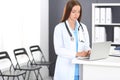 Doctor woman at work. Portrait of female physician using laptop computer while standing near reception desk at clinic or Royalty Free Stock Photo