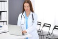 Doctor woman at work. Portrait of female physician using laptop computer while standing near reception desk at clinic or Royalty Free Stock Photo