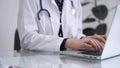 Doctor woman is working with laptop computer at the glass table in clinic. Physician is typing medical information or