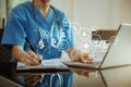 Doctor working on laptop computer, writing prescription clipboard with record information paper folders on desk in clinic,