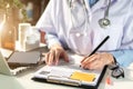 Doctor working on laptop computer, writing prescription clipboard with record information paper folders on desk. Royalty Free Stock Photo