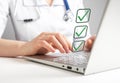 Doctor working on laptop and taking survey, ticking answers at screen. Woman in lab coat sitting at table with computer Royalty Free Stock Photo