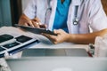 Doctor working on tablet, writing prescription clipboard with record information paper folders on desk in clinic, Healthcare and Royalty Free Stock Photo