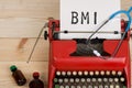 doctor workplace with blue stethoscope, pills, red typewriter with text BMI Body mass index