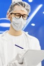 A doctor in white gloves, a protective mask and glasses makes notes on the patientÃ¢â¬â¢s card Royalty Free Stock Photo