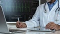 Doctor writing clinical notes while analyzing patient's ECG data on a digital monitor Royalty Free Stock Photo