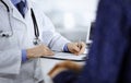 A doctor is writing a medical prescription for his patient, while sitting together at the desk in the cabinet in a Royalty Free Stock Photo